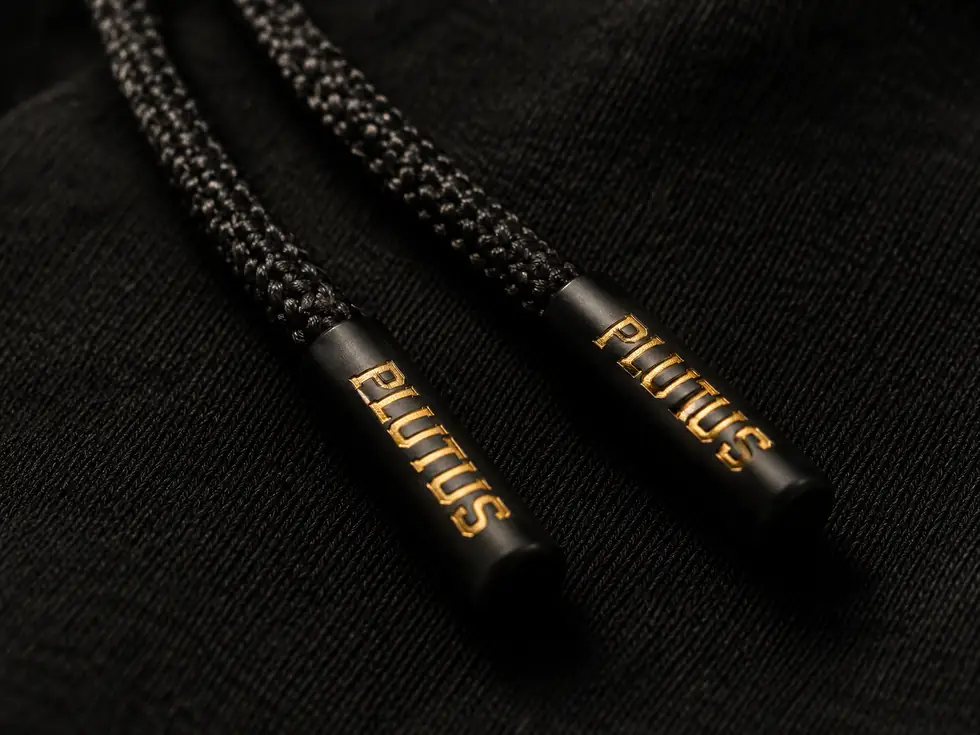 Hoodie drawcords with gold PLUTUS tips on black fabric.