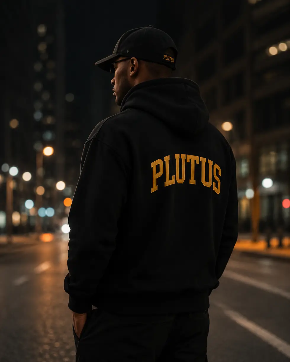 The back of a black PLUTUS hoodie on a city street at night.